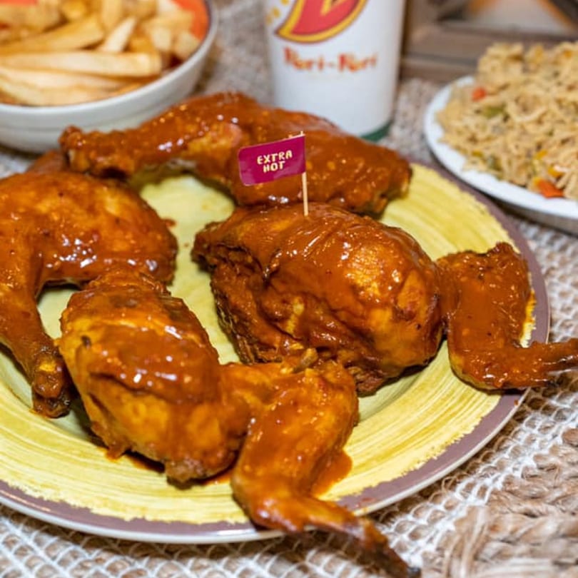 Peri Peri Original extra hot chicken pieces on a plate with fries and rice in the background.