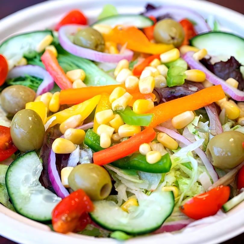 Close-up of a vibrant Peri Peri Original Portuguese salad with olives, corn, peppers, and cucumber.